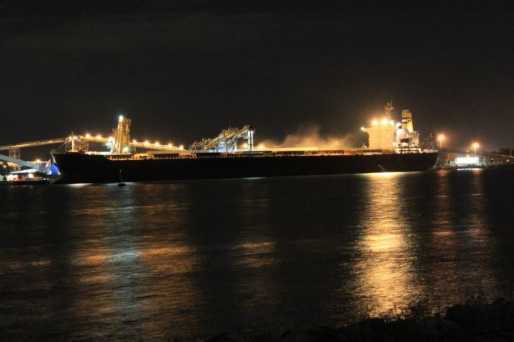 A bulk carrier loading grain at a port terminal at night